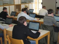 In einem Klassenzimmer sitzen mehrere Erwachsene vor ihren Laptops.