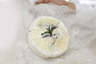 Auf der Oberseite eines runden Weichkäses mit Weißschimmel prangen Kräuter und Blüten - Rosmarin, Zitronenmelisse und Lavendel.