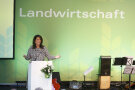 Staatsministerin Michaela Kaniber steht am Rednerpult, hinter ihr befindet sich eine grüne Wand mit der weißen Aufschrift "Landwirtschaft".