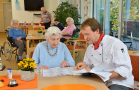 Koch bietet Teller mit Essen Seniorin an