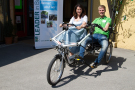 Zwei Personen auf einem Tandem, bei dem zwei Schalensitze nebeneinander angeordnet sind