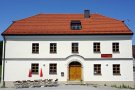 Zweigeschossiges Gasthausgebäude mit weißer Fassade, Krüppelwalmdach und sechsfelderigen Sprossenfenstern. Zweiflügelige Haustüre aus Holz mit Rundbogen