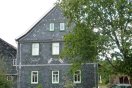 Giebelansicht des sanierten Satteldachbaus mit Schieferfassade in Spitzwinkelschablonen