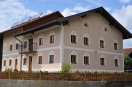 Saniertes zweigeschossiges Bauerhaus mit altrosa Fassade und quadratischen Sprossenfenstern. Fensterumrahmung und Bänderungen in weißer Farbe