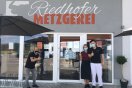 Vor einer Metzgerei stehen zwei Männer und eine Frau