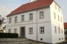 Saniertes zweigeschossiges Schul- und Rathausgebäude mit weißer Fassade, barockem Krüppelwalmdach und vierfelderigen Sprossenfenstern. Fensterumrahmung und Bänderungen in grauer Farbe