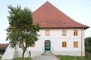 Zweigeschossiger, weißer Baukörper mit Walmdach. Sechsfelderige Sprossenfenster, umlaufende graue Bänderung betont die Zweigeschossigkeit in der FassadeDe Grosskoellnbach 2
