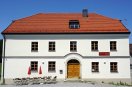 Zweigeschossiges Gasthausgebäude mit weißer Fassade, Krüppelwalmdach und sechsfelderigen Sprossenfenstern. Zweiflügelige Haustüre aus Holz mit Rundbogen