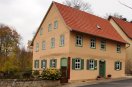 Zweigeschossiges verputztes Fachwerkhaus, sechsfeldrigen Sprossenfenstern, Fassade in zartem rötlichem Erdton. Grüne Fensterläden und Türe