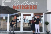 Vor einer Metzgerei stehen zwei Männer und eine Frau
