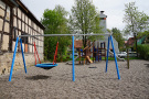 Spielplatz mit Schaukeln und Klettereinrichtungen. Im Hintergrund Feuerwehrhaus.