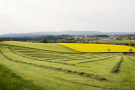 Agrarlandschaft im Vordergrund. Am Horizont Dorf mit bewaldetem Höhenzug.