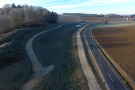 Detailansicht des langgezogenen und geschwungenen Rückhaltebeckens entlang der Straße. Um das Becken führt ein geschotterter Wirtschaftsweg.