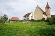 Begrünte Freifläche vor der Kirche und dem Pfarrhaus, die zum Dorfplatz umgestaltet werden soll