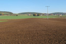 Frisch angelegte Flache Bodenwelle; im Hintergrund Wiesen und ein Dorf