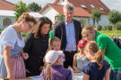 Landwirtschaftsministerin Michaela Kaniber und Kultusminister Michael Piazollo stehen mit zwei Frauen und vier Kindern aneinem Tisch und schauen auf etwas.