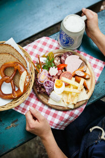 Blick von oben auf ein Brotzeitbrett mit Wurst und Käse. Daneben steht ein Bierkrug.