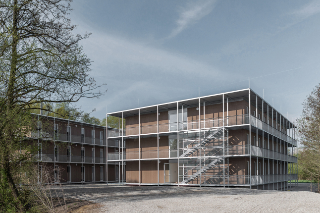 Quaderförmiger Holzbau mit umlaufenden Balkonen und Außetreppen aus Metall (© Andreas Kern)