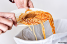 Hände, die mithilfe einer Gabel Spaghettireste in den Abfall geben