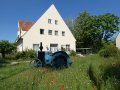 hostorischer Traktor auf einer Blühfläche vor einem Gebäude