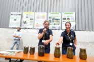 Dr. Katrin Harms und Barbara Misthilger stehen mit Mikrofon hinter einem Tisch, auf dem große gefüllte Gläser aufgereiht sind.