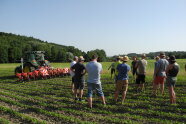 Gruppe im Gespräch auf einem Sojafeld neben Traktor mit Foto-Hacke.