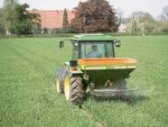 Ein Traktor mit Streuvorrichtung fährt über ein Feld.