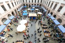 Blick von oben auf einen Innenhof mit zahlreichen Verkaufsständen und Besuchern