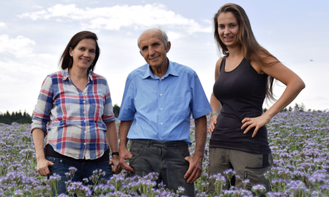 zwei Frauen und ein Mann stehen in einem blühenden Phacelia-Feld. Foto: Biohof Lex