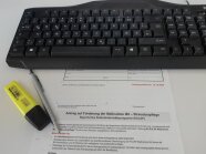 Förderantrag und Stifte vor einer Tastatur.