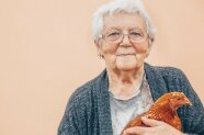 Lächelnde Dame hält ein Huhn in den Händen
