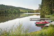 Angelegte Tret- u. Paddelboote in einem Fluss im Grünen neben einem Holzsteg.