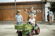Kinder im Bauernhof spielen fröhlich mit einem Spielzeugtraktor