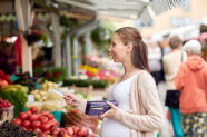 Junge Frau mit Karte in der Hand auf einem Markt beim bargeldlosen Bezahlen