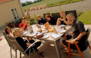 Eine Bauernfamilie sitzt auf der Terrasse an einem großen Tisch beim Essen.