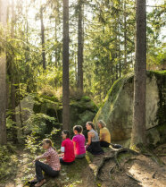 Vier Frauen sitzen zwischen großen natürlichen Steinen in einem mit Licht durchfluteten Wald