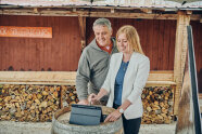 Lächelnd sehen eine Frau und ein Mann in ein Tablet, das auf einem Holzfass steht