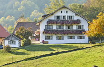 Ein großes Haus mit geschmückten Balkons und Fensterläden in ländlicher Umgebung im Abendlicht.