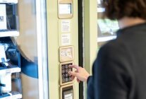 Eine Frau steht vor einem Verkaufsautomaten stehend und tippt auf ein Bedienfeld