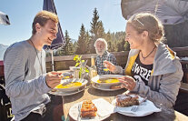 Ein junges Paar sitzt in einem Lokal im Freien. Beide haben Essen vor sich auf dem Tisch.