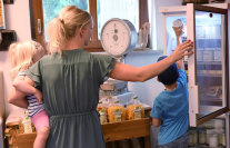 Eine Frau mit zwei Kindern öffnet einen Selbstbedienungs-Kühlschrank.