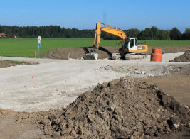 Ein Bagger schüttet eine neue Straße durch einen Acker auf.