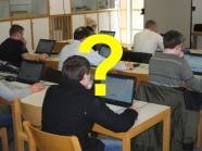 Blick in einen Klassenraum, Schüler sitzen an Tischen. Darüber ein gelbes Fragezeichen.