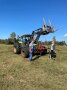 Traktor mit Zwillingsreifen und zwei Ballengabeln als Anbau. Davor stehen ein Landwirt und Frau Woortman mit Ihrem Hund.