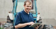 Ein Landwirt steht mit dem Tablet in der Hand vor einem Traktor.