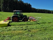 Ein Traktor mit Front-Heck-Mähwerksgespann mit Sensosafe Assistenzsystem mäht eine Grünlandfläche.