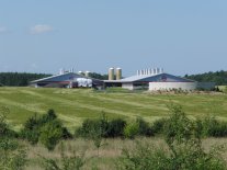 Ansicht auf ein Stallgebäude im Außenbereich mit Güllerundbehälter und Getreidefeld