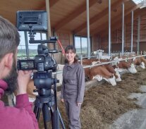 Eine Frau steht vor einer Kamera in einem Milchviehstall.