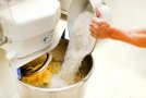 Hände schütten Mehl in eine Küchenmaschine mit Teig