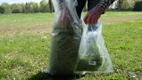 Mann nimmt aus einem Sack Gras an verschiedenen Stellen heraus und tut es in eine separate Tüte